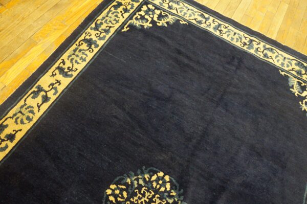Dark blue rug with a yellow and teal scroll border rests on shiny golden hardwood floors.