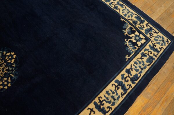 A navy blue rug with a tan and indigo floral scroll border lies on wood flooring.