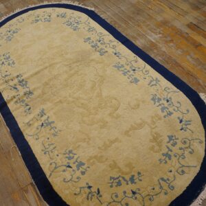 A tan oval rug with pale blue scrollwork and a navy border lies on distressed wooden flooring.