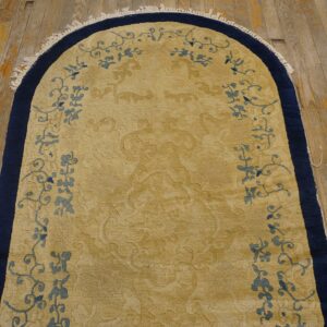 Gold arched rug with navy border and blue floral motifs lies on distressed wood flooring.