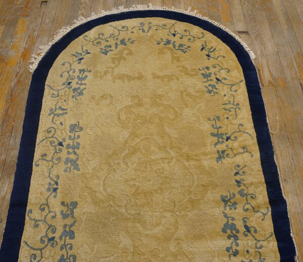 Gold arched rug with navy border and blue floral motifs lies on distressed wood flooring.