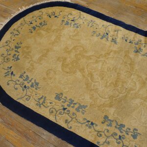 Oval gold rug with navy blue edges and blue scrolling floral border on hardwood planks.
