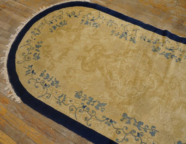 Oval gold rug with navy blue edges and blue scrolling floral border on hardwood planks.