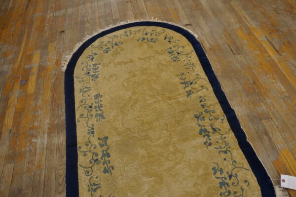 Arched golden rug with scrolling blue motifs and a navy border on worn wood flooring.