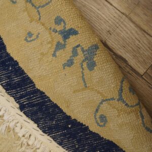 Textured tan and blue patterned rug with fringe, partially curled on light brown wooden flooring.