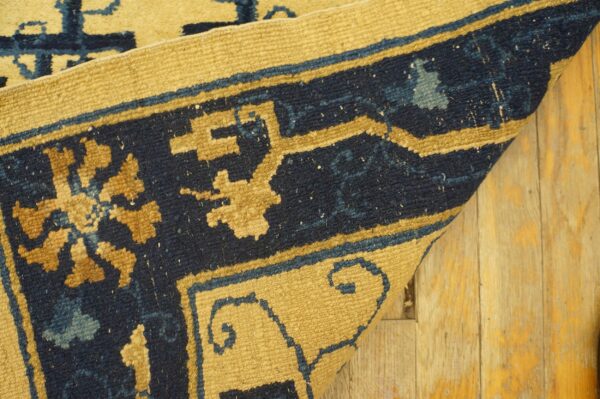A curled rug corner features navy blue and golden geometric patterns on rustic light wood floors.