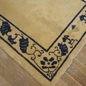 Beige rug with thick navy blue floral and geometric border shown on distressed wooden planks.