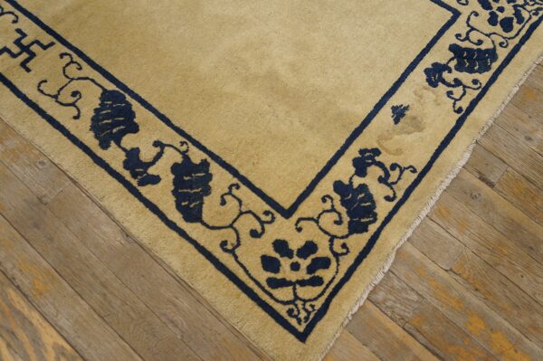 Beige rug with thick navy blue floral and geometric border shown on distressed wooden planks.