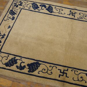 Tan rug with dark blue vine and swastika borders rests on distressed wooden plank flooring.