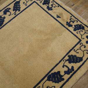 A tan rug with a dark blue scrolling vine border is placed on distressed wooden floors.