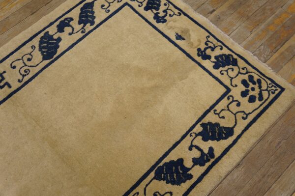 A tan rug with a dark blue scrolling vine border is placed on distressed wooden floors.