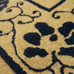 Detailed view of the rug's short pile texture, featuring navy blue scrolling designs on mustard yellow.