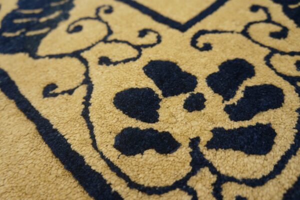 Detailed view of the rug's short pile texture, featuring navy blue scrolling designs on mustard yellow.