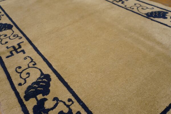 Close-up of a tan rug with a dark blue traditional border pattern, including geometric symbols.