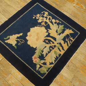 Navy square rug with a central beige and green floral motif on diagonal wooden planks.