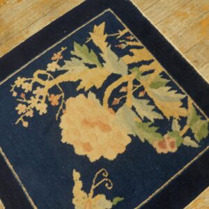 Navy blue floral square rug with gold and sage accents on worn wooden floorboards.