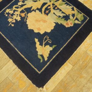 Navy blue square rug corner featuring large cream and green floral designs on light distressed wood floorboards.