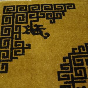 Black key pattern borders a mustard yellow high-pile rug lying on distressed wood planks.