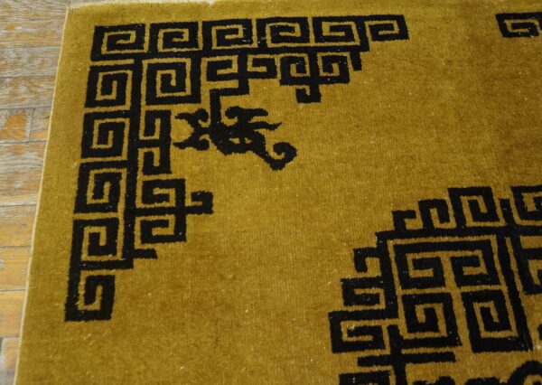 Black key pattern borders a mustard yellow high-pile rug lying on distressed wood planks.