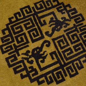 Mustard yellow rug detail featuring a large black geometric medallion with mythical figures inside.