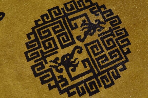 Mustard yellow rug detail featuring a large black geometric medallion with mythical figures inside.
