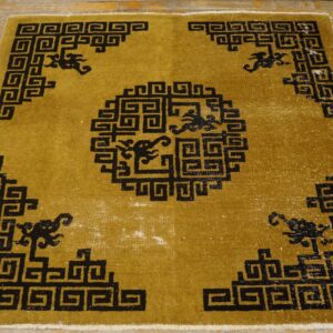 Gold and black rug with a geometric spiral design and stylized figures rests on distressed wood floor.