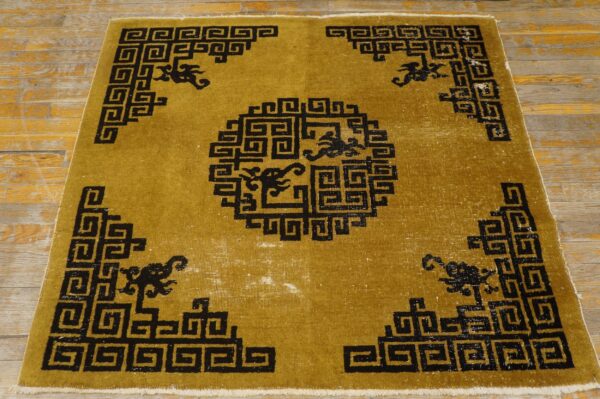 Gold and black rug with a geometric spiral design and stylized figures rests on distressed wood floor.