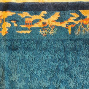 Teal rug detail showing a carved floral field and a high-contrast orange and gold border design.