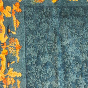 Textured teal rug features an embossed tone-on-tone floral field next to a vibrant orange abstract border and navy edge.
