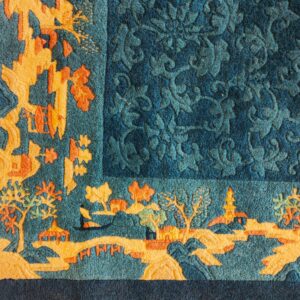 Teal and orange rug corner featuring a carved scenic border and a tone-on-tone blue floral main field.