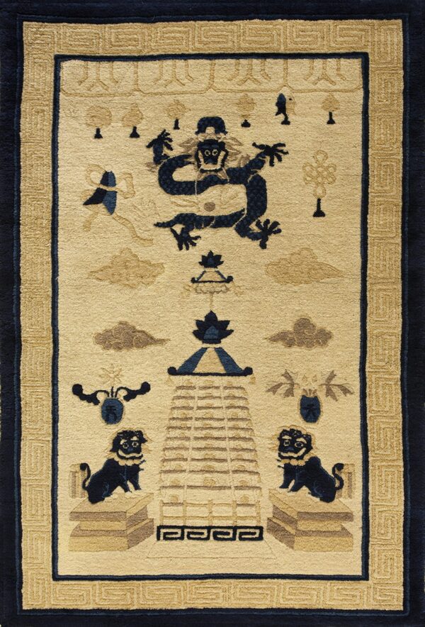 Cream rug featuring a central navy blue creature motif, taupe clouds, and an ornate tan meander border.