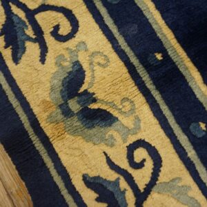 Textured navy, beige, and sage rug displaying floral scrollwork next to light brown wood flooring.