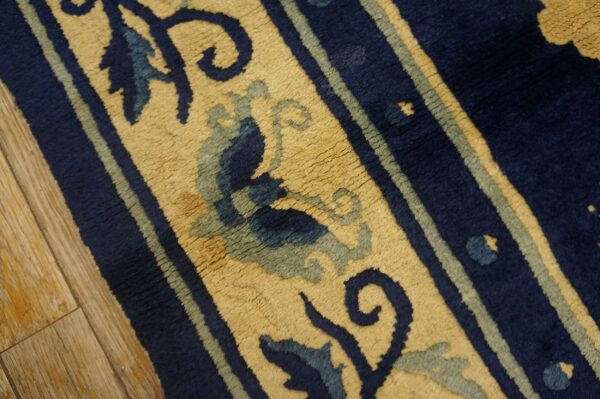 Textured navy, beige, and sage rug displaying floral scrollwork next to light brown wood flooring.