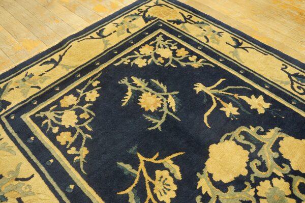 A corner of a navy blue rug with gold and sage floral patterns lies on light hardwood plank flooring.