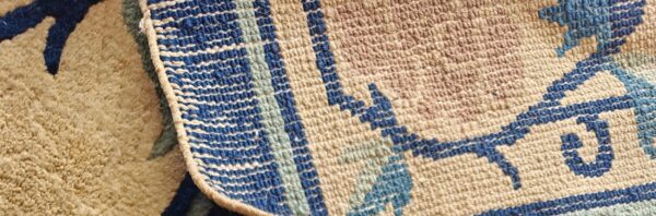 A rug detail contrasts tan high pile texture with a geometric low loop border in blue and beige.