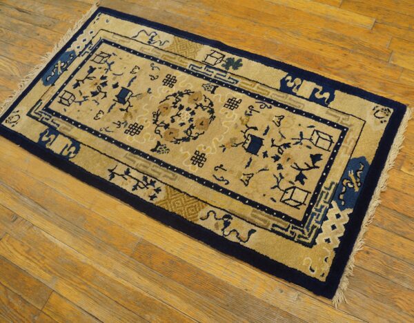 A small tan and navy rug with geometric and floral patterns lies on a distressed wood floor.