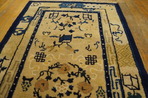 Beige rug with navy blue and gold traditional patterns, featuring geometric borders on hardwood floor.