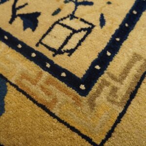 Corner detail of a plush yellow rug with navy blue and tan traditional border design.