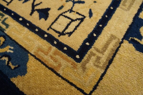 Corner detail of a plush yellow rug with navy blue and tan traditional border design.
