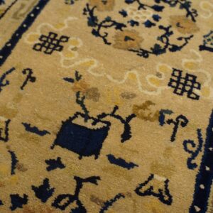 Closeup of a tan rug with navy blue geometric symbols and gold floral patterns.
