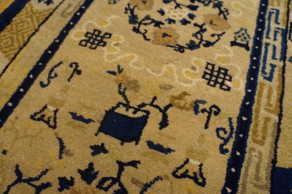 Closeup of a tan rug with navy blue geometric symbols and gold floral patterns.