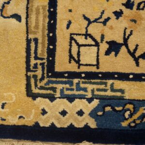 Close-up of a golden tan rug featuring navy and teal blue stylized patterns on distressed wood flooring.