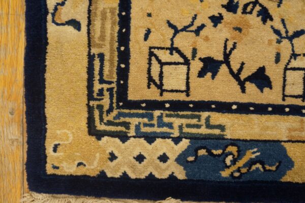 Close-up of a golden tan rug featuring navy and teal blue stylized patterns on distressed wood flooring.