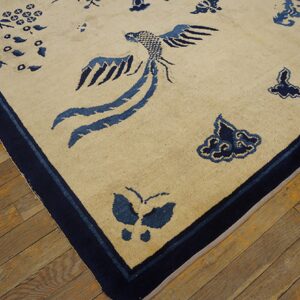 A tan rug with a dark blue bird and butterfly pattern lies on distressed wooden floor planks.