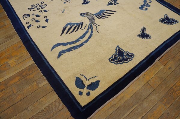 A tan rug with a dark blue bird and butterfly pattern lies on distressed wooden floor planks.