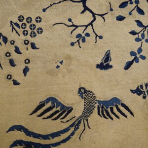 A light tan rug detailed with dark blue designs of a bird, flowering branches, and butterflies on wood flooring.