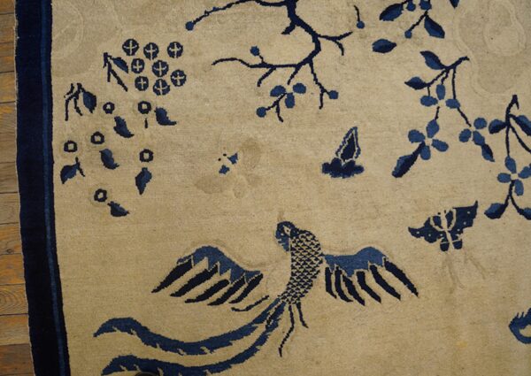 A light tan rug detailed with dark blue designs of a bird, flowering branches, and butterflies on wood flooring.