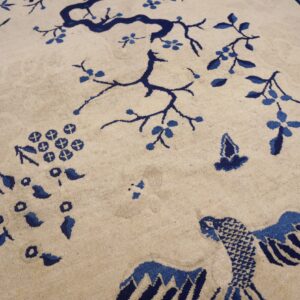 Cream rug with a blue border, featuring branches, bamboo, and bird designs on wood flooring.