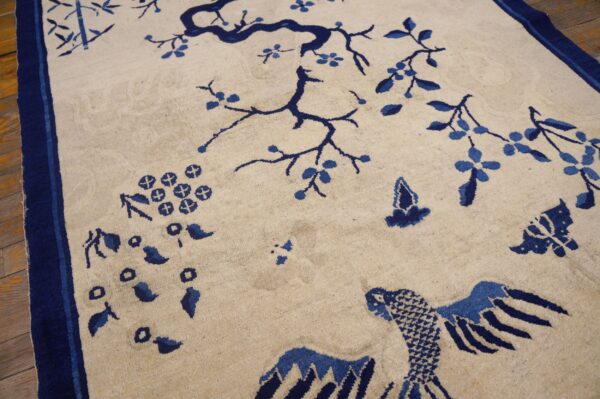 Cream rug with a blue border, featuring branches, bamboo, and bird designs on wood flooring.