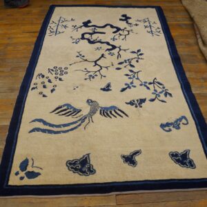 Beige rug with blue stylized bird, tree, and floral motifs, displayed on warm wooden flooring.